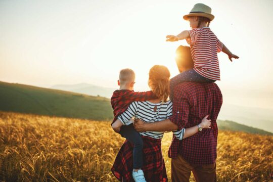 Una familia reunida en un campo contemplando una puesta de sol dorada.