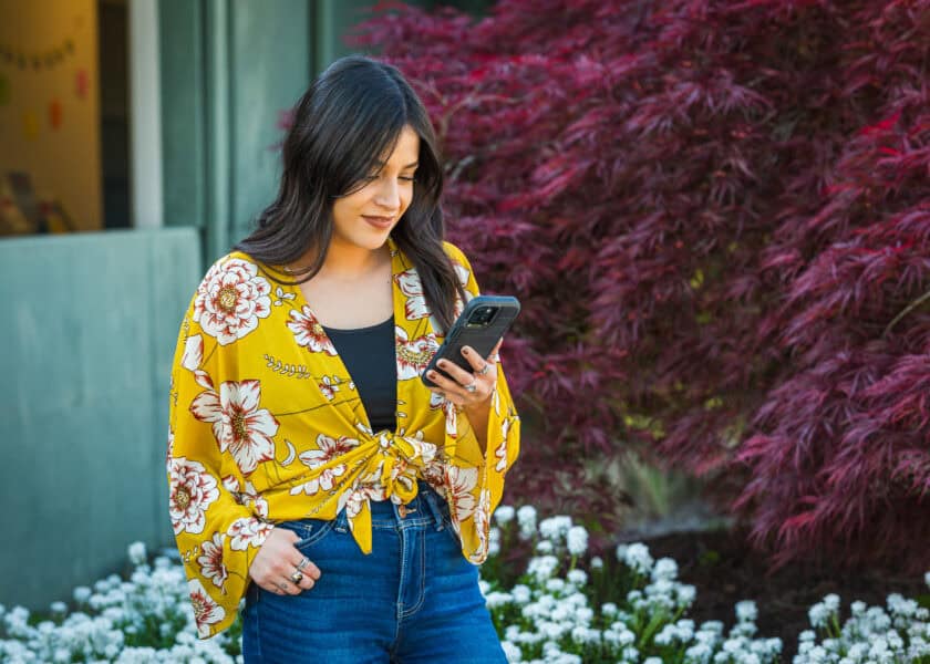 A woman in a yellow shirt looking at her phone and smiling