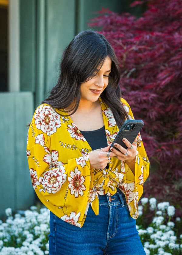 A woman in a yellow shirt looking at her phone and smiling