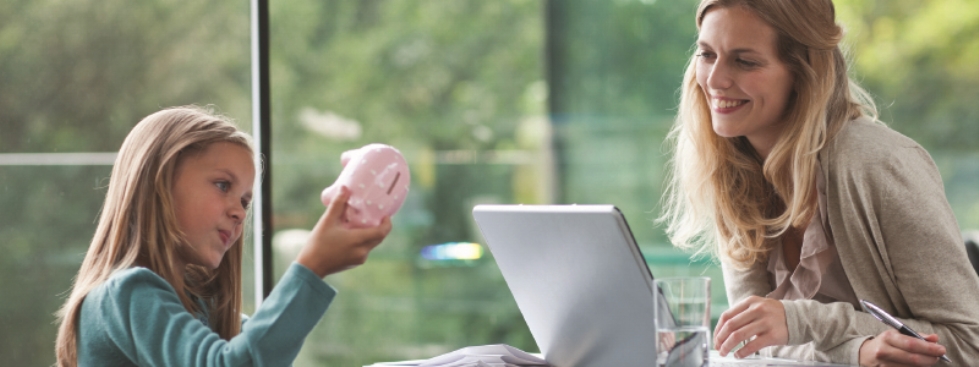A girl playing with a piggy bank while a woman works at a laptop