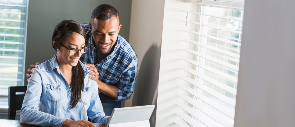 A happy young couple by a window looking at their budget on a laptop
