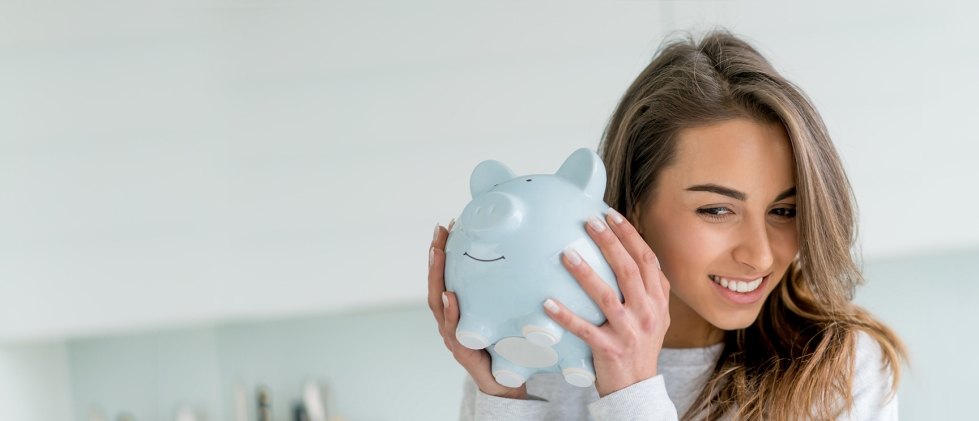 A woman shaking a piggy bank close to her ear