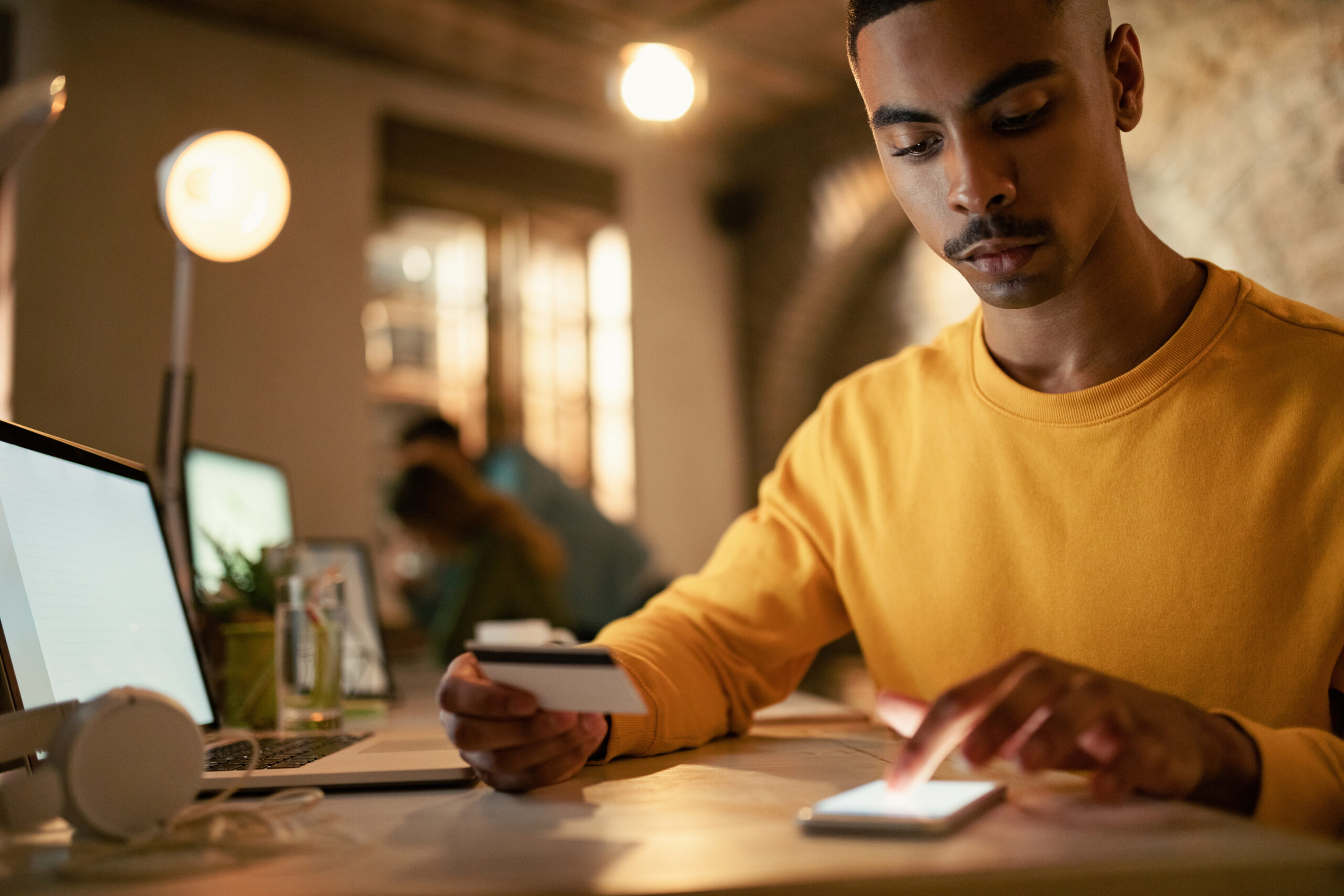 Young man using credit cart and mobile phone while checking his online bank account