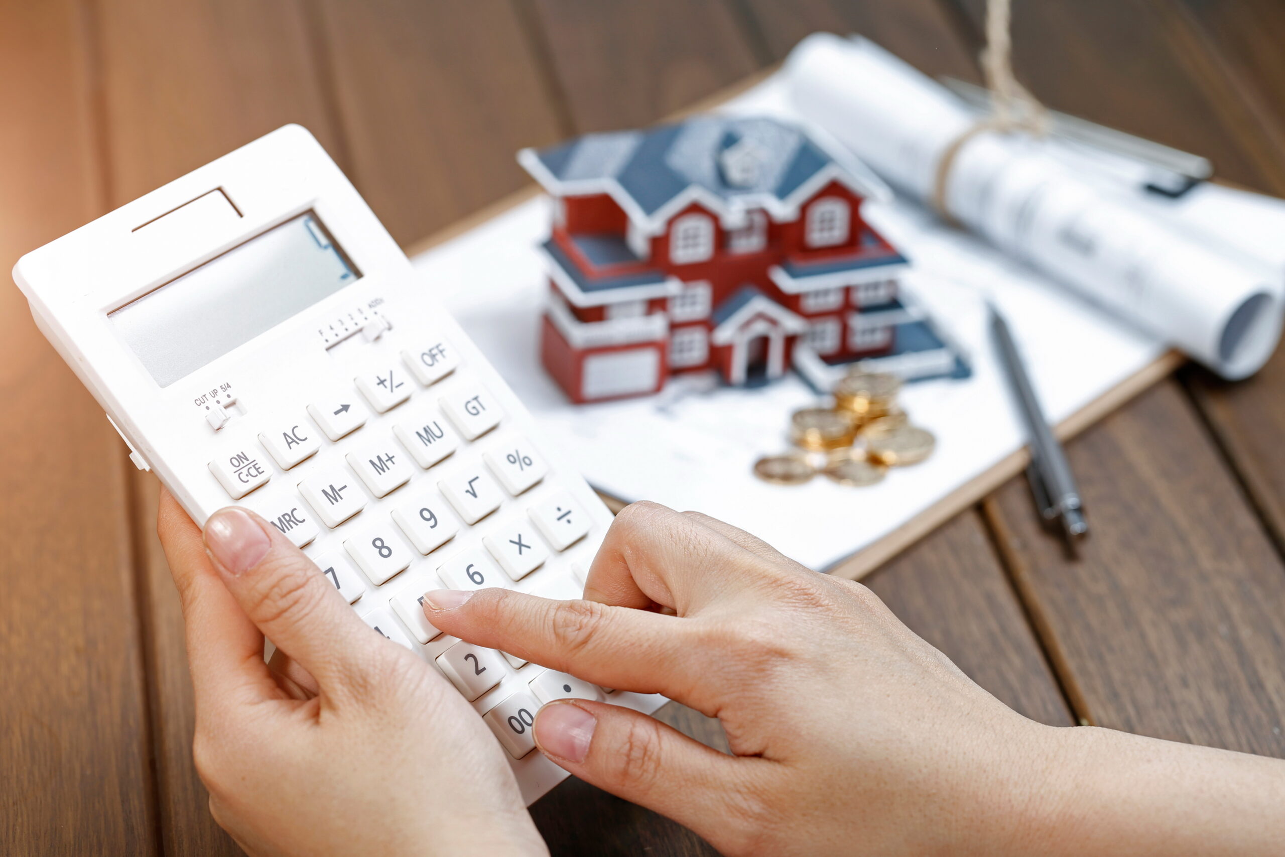 photo a female hand operating a calculator in front of a villa house model