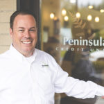 Man smiling in front of a Peninsula sign