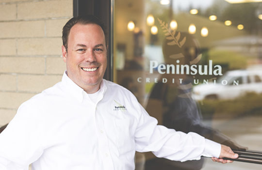 Man smiling in front of a Peninsula sign