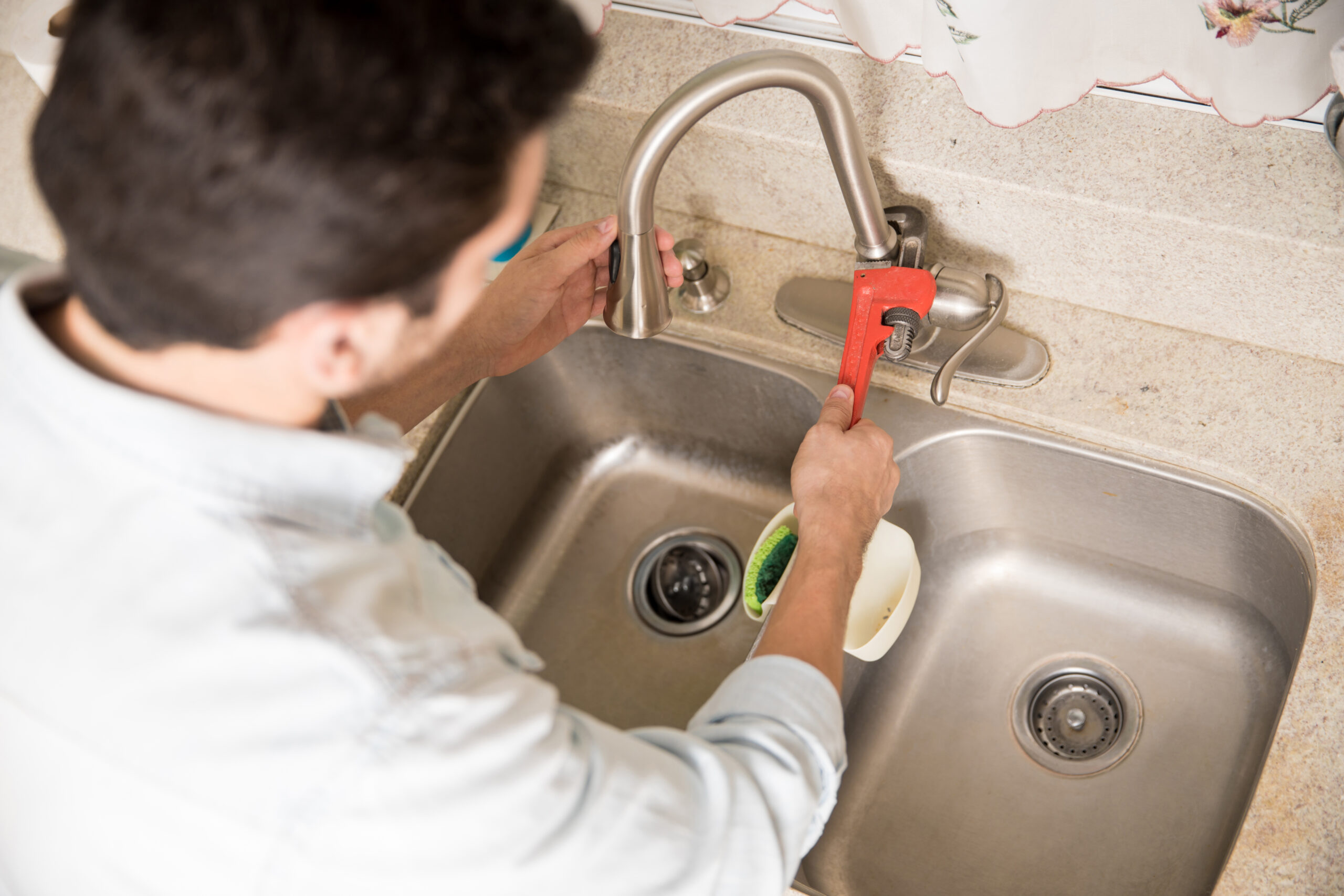 Male plumber using a wrench to tighten a water faucet in a kitchen, seen up close