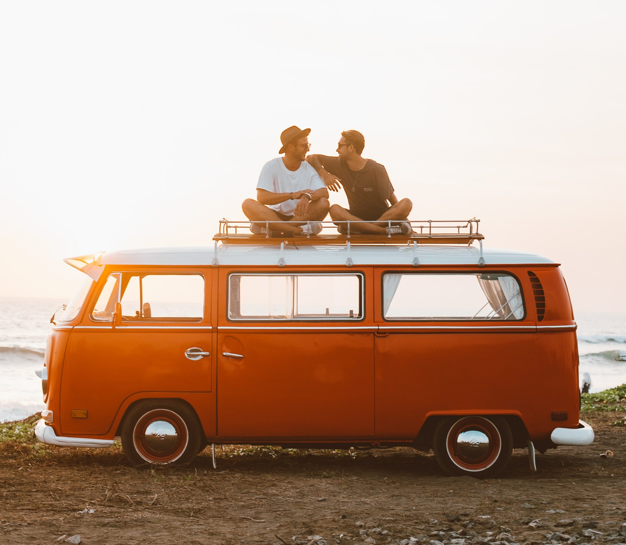 Two friends sitting on top of a camper van on the beach